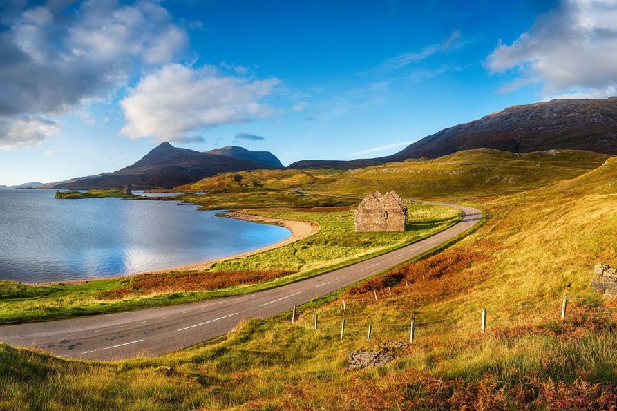 Autumn at Loch Assynt in Scotland with the ruins of Calda House and Ardvreck Castle in the far left, landmarks on the NC500 scenic driving route