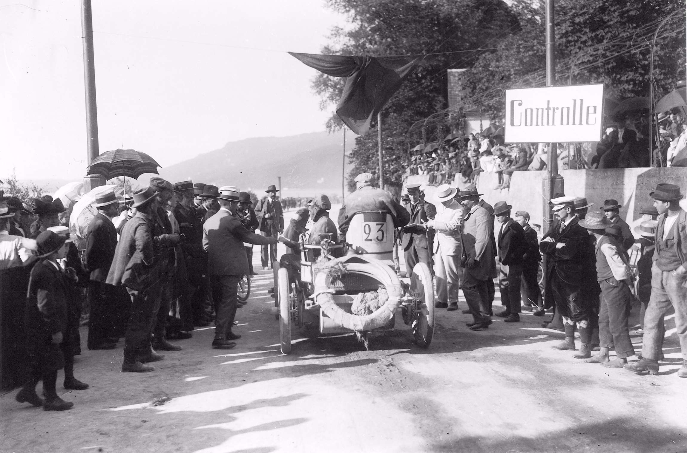 Paris-Vienna race control in Switzerland - Cechamps aboard his Dechamps - differing modes of dress denote social strata - boaters are worn by senior officials - note straw-hatted bare-foot urchin on right
