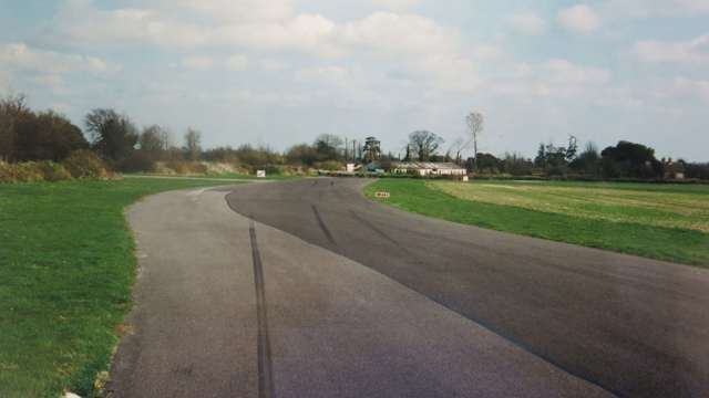 Woodcote Corner approach as it used to be, patchy surface, sloping earth banks, and some advisory track boards