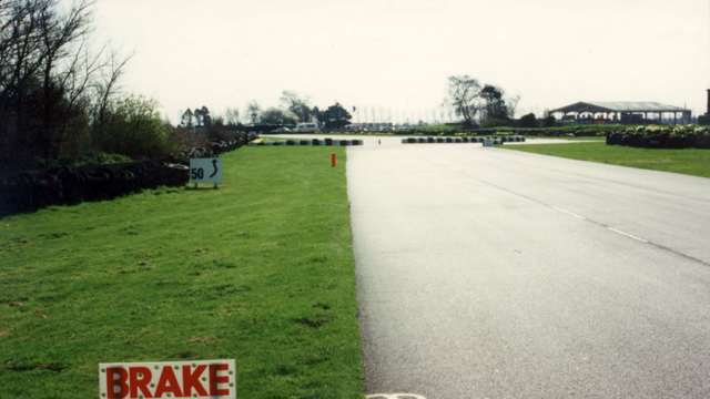 Chicane approach after Woodcote Corner with the old tyre chicane barrier arranged across the road and at the right-side apex ahead.  To the left stands the ‘jungle’ that existed in 1997 - it would have totally blocked spectators’ view today...
