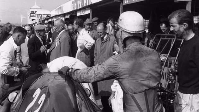 Travel-stained Tony Brooks (right) looks on as Stuart Lewis-Evans’s third-string Vanwall is investigated in the 1957 British GP pits - Tony Vandervell beyond the stooped mechanic...