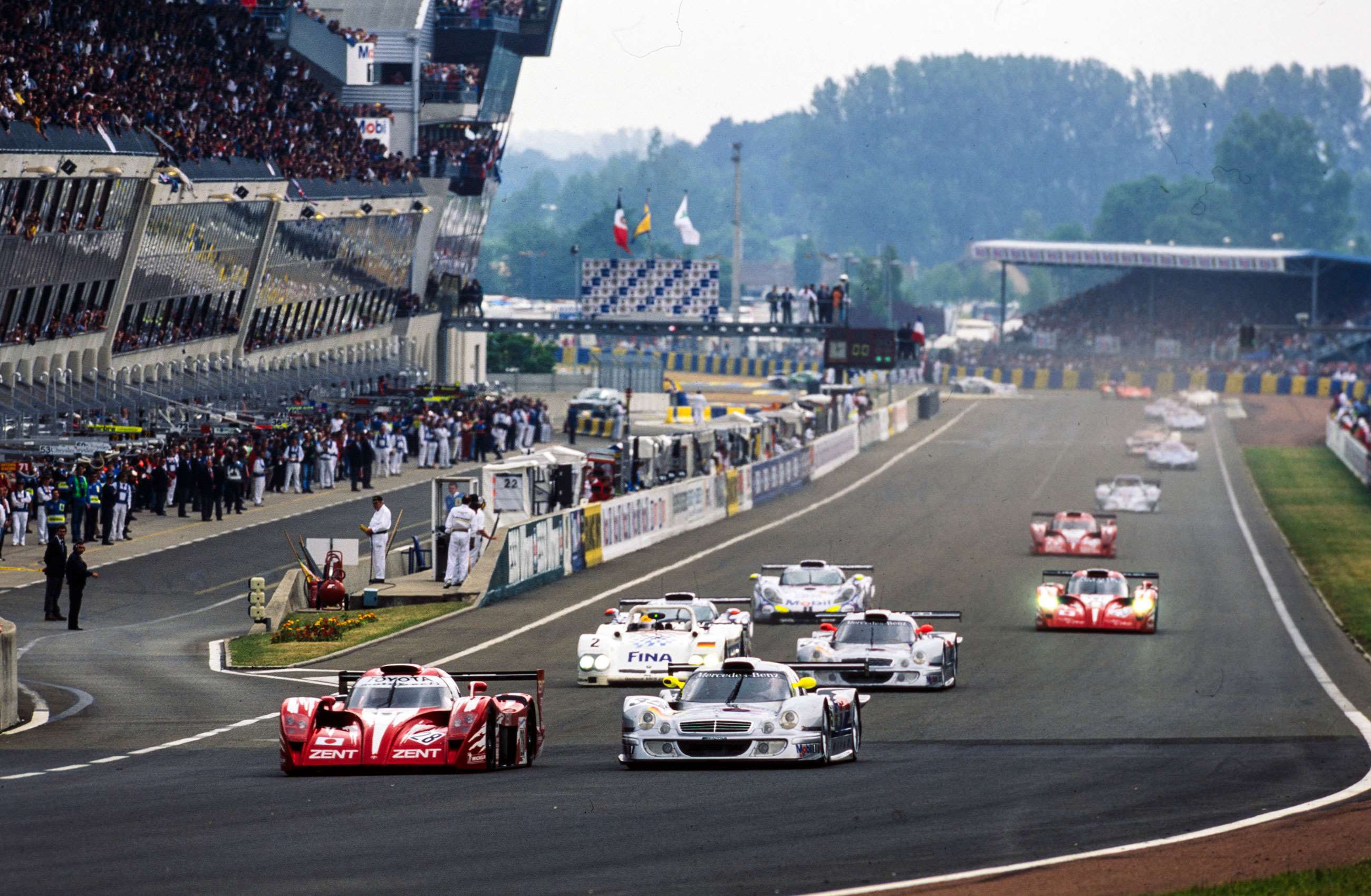 The race start of the 1998 Le Mans 24 Horus, with the Mercedes-Benz CLK LM front and centre, flanked by a Toyota GT-One. 
